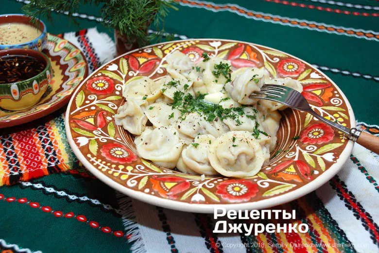 Готові домашні пельмені в кольоровій мисці з травами