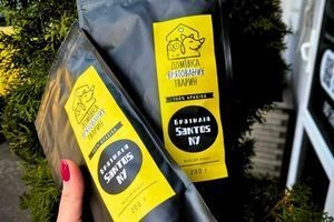 Дві упаковки меленої кави в руках на фоні листя